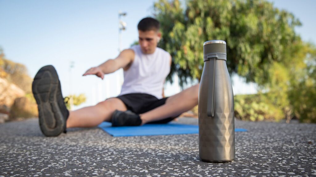 water bottle on the pavement in the front, and a man stretching on a mat in the back