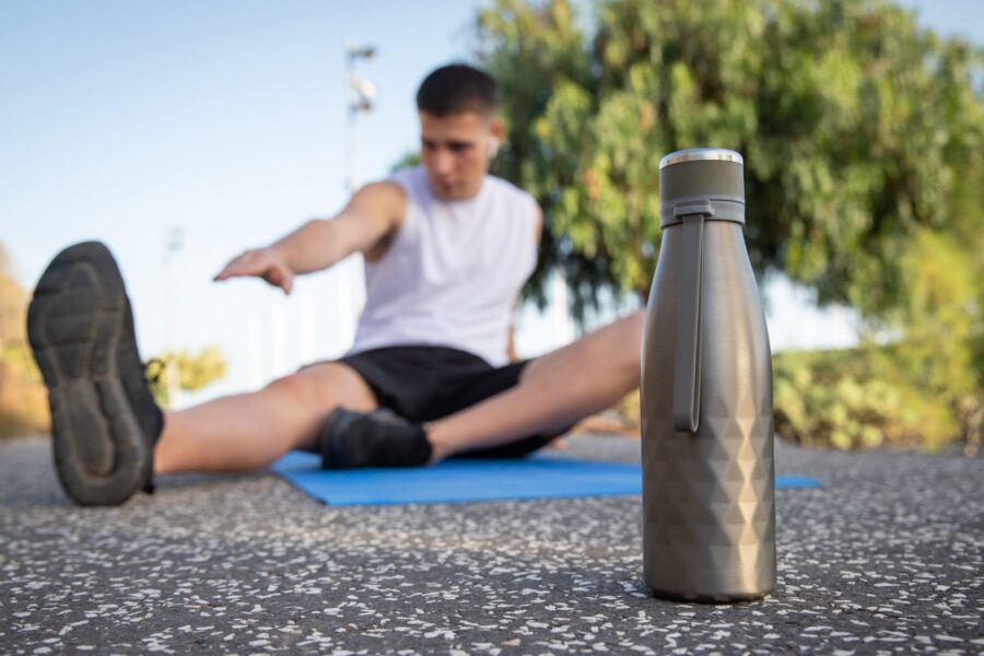 water bottle on the pavement in the front, and a man stretching on a mat in the back