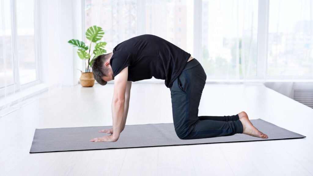 Man doing the Cat Pose as morning stretching on a grey mat indoors