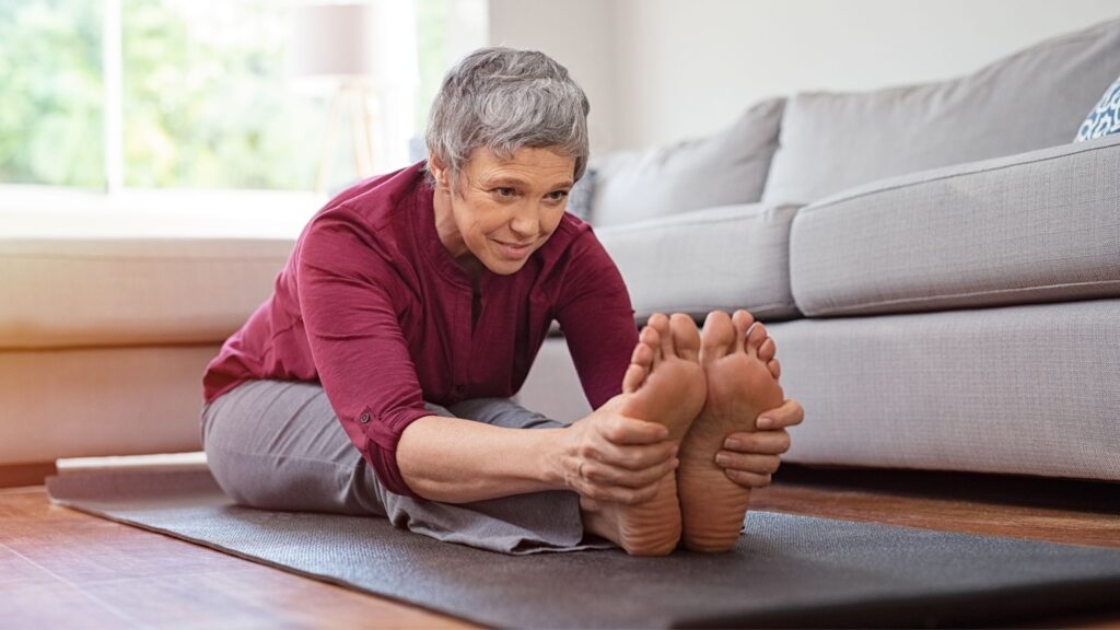 senior woman doing stretching exercise while sitting on a yoga mat at home